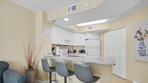 A modern kitchen with white cabinets, a granite countertop, and a bar area with stools. - Oceanview 1BR Suite + Lazy River & Hot Tub (Myrtle Beach)