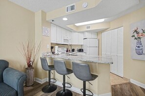 Eine moderne Küche mit weißen Schränken, einer Arbeitsplatte aus Granit und einer Bar mit Hockern.