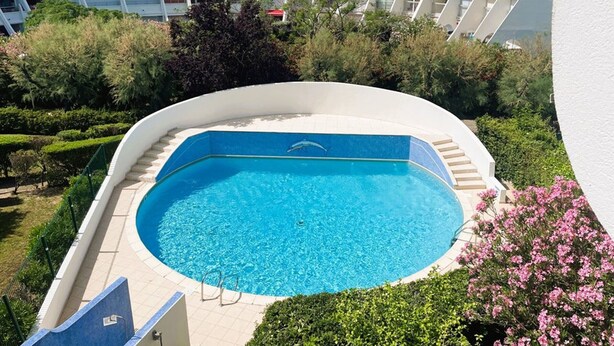 Una piscina con acqua cristallina azzurra, circondata da un solarium bianco e una scalinata che conduce verso il basso.