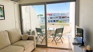 Una stanza con un divano, un tavolo con un portatile e vista su un balcone con sedie e un tavolo.