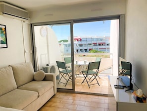 Ein Zimmer mit einer Couch, einem Tisch mit einem Laptop und Blick auf einen Balkon mit Stühlen und einem Tisch.