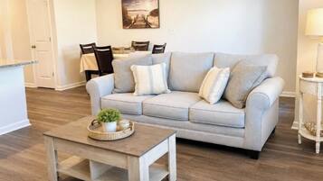 A living room with a sofa, coffee table, and a dining area with chairs and a table.