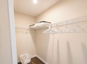 Un petit placard bien rangé, avec deux étagères et une tringle à vêtements, un panier blanc et un plancher en bois.