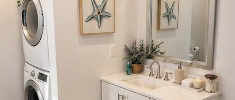 A modern bathroom with a washing machine, a sink, a mirror, and decorative starfish.