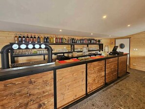 Uma área de bar com balcão de madeira, diversos frascos de bebidas e uma máquina de café.