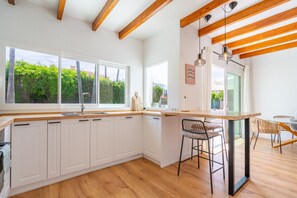 A modern kitchen with white cabinets, wooden beams, large windows, and a bar area with stools. - Mar - with private swimming pool (LLucmajor)