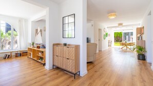 Una habitación amplia con suelo de madera, un armario empotrado, un ventanal con cortinas y una zona de comedor con mesa y sillas.