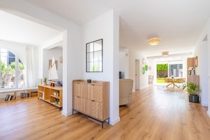 A spacious room with wooden flooring, a built-in cabinet, a large window with curtains, and a dining area with a table and chairs. - Mar - with private swimming pool (LLucmajor)