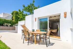 A modern outdoor patio with a wooden table and chairs, a glass door leading to an interior space, and a white exterior wall. - Mar - with private swimming pool (LLucmajor)