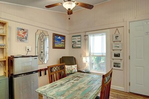 Un área de comedor con una mesa de madera, sillas, un ventilador de techo y obras de arte colgadas en la pared.
