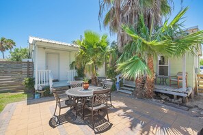 Eine Terrasse mit rundem Tisch und Stühlen, ein kleines weißes Gebäude und Palmen.
