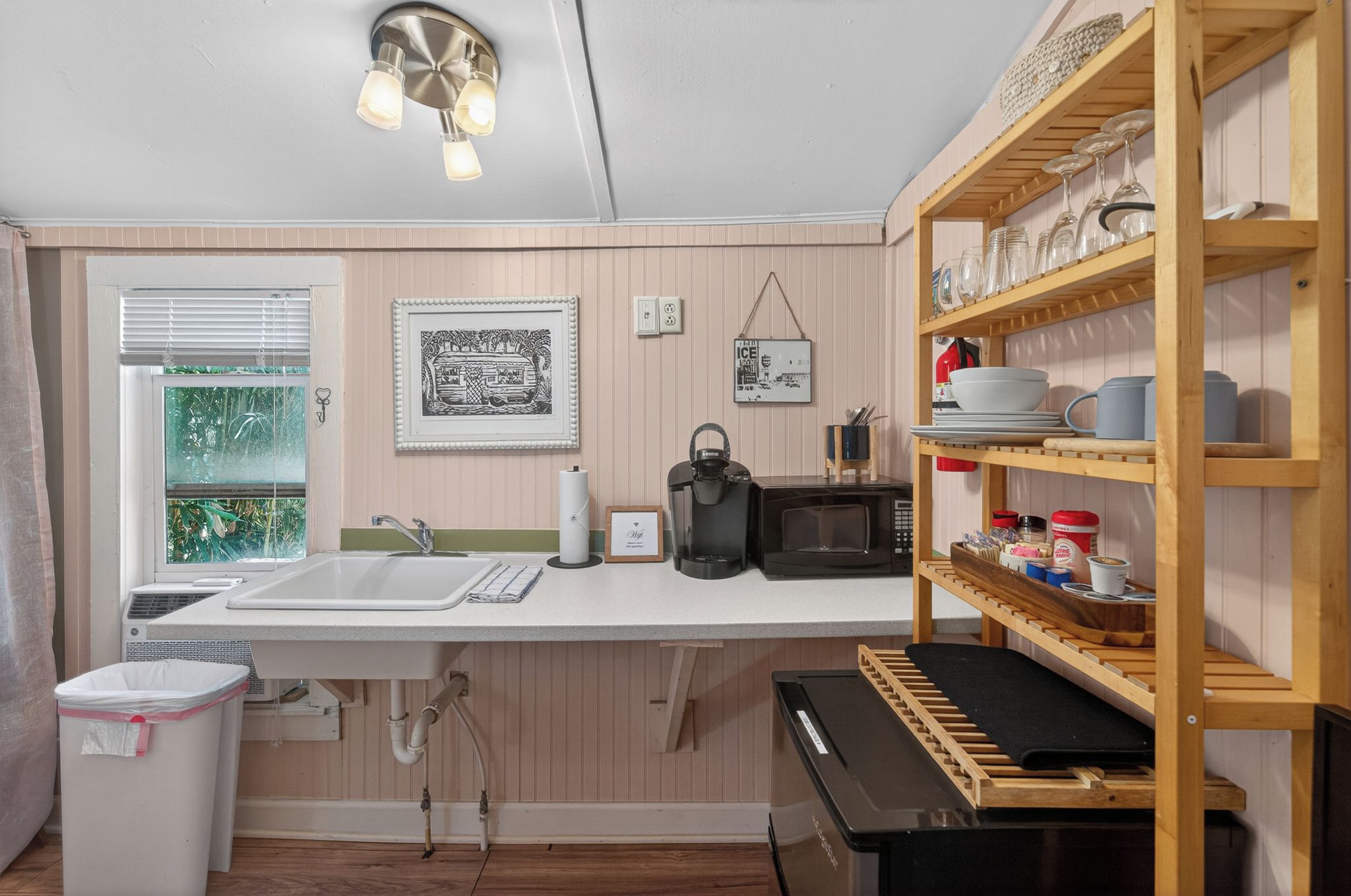 A compact kitchen with a sink, microwave, and wooden shelves.