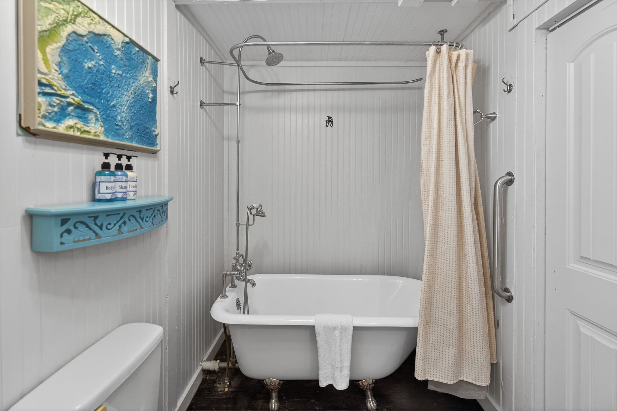 A bathroom with a white bathtub, a shower curtain, a towel hanging on the tub, and a shelf with bottles.