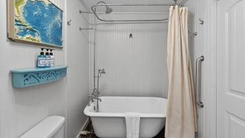 A bathroom with a white bathtub, a shower curtain, a towel hanging on the tub, and a shelf with bottles.