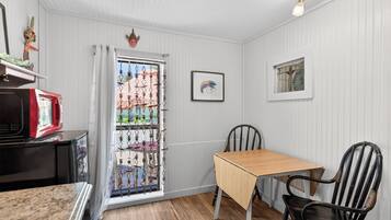 Een kamer met een houten tafel, twee stoelen, een raam met decoratieve gordijnen en een lijst met een afbeelding aan de muur.