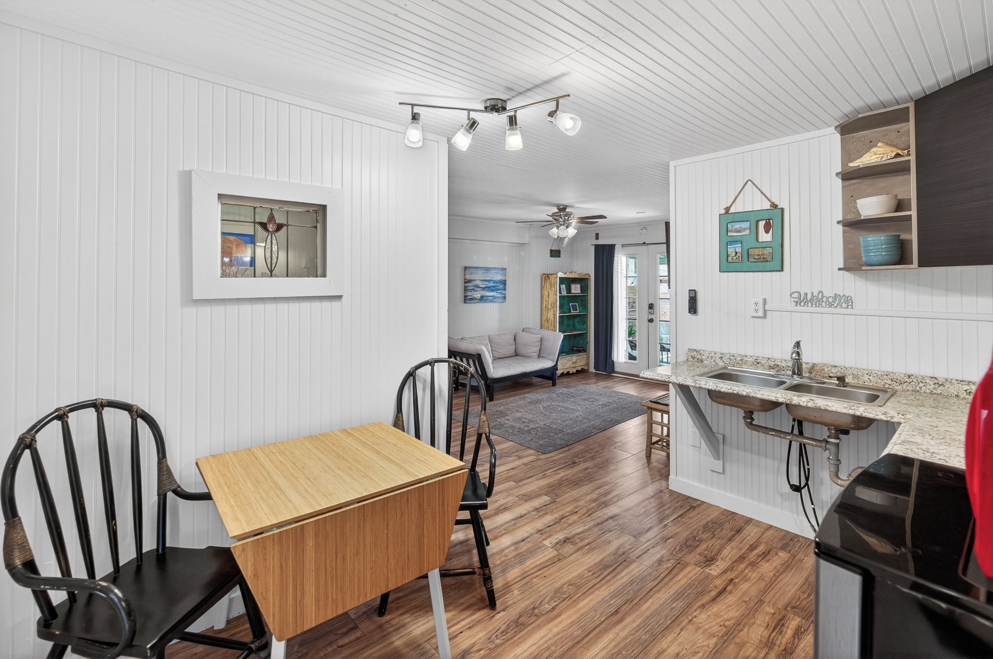 A compact kitchen with a wooden table and chairs, a built-in sink, and a ceiling fan.