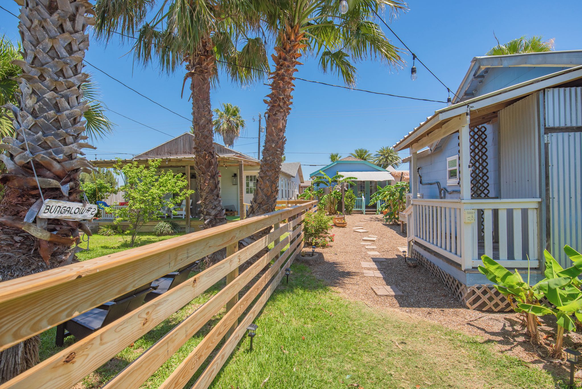A bungalow with a wooden deck, palm trees, and a clear sky.