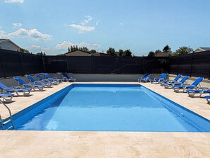 Una piscina rectangular con agua azul, rodeada por un solárium con baldosas.