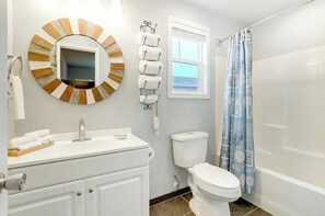Une salle de bain avec un miroir rond, des toilettes, un lavabo et un rideau de douche.