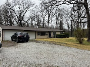 Une maison de plain-pied avec un garage, une allée en gravier et une pelouse.