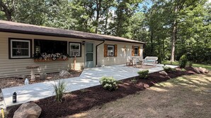 A single-story house with a front porch, a small garden area with mulch and plants, and a bench. - Cozy Cottage on 9 tranquil acres in Wright City, Mo. Minutes to wedding venues! (Wright City)
