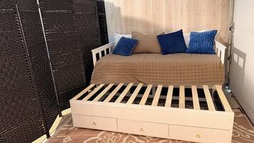 A single bed with a wooden frame and a quilted cover, accompanied by two pillows, in a room with a patterned floor and a wooden partition.