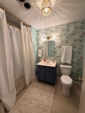 Une salle de bain avec un rideau de douche, un lavabo avec un miroir, des toilettes et un mur décoré de motifs.