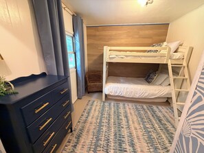 Une chambre avec un lit superposé, une commode, une petite chaise et un tapis à motifs.