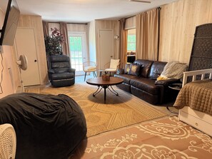 A living room with a sofa, chairs, a coffee table, and a bed.