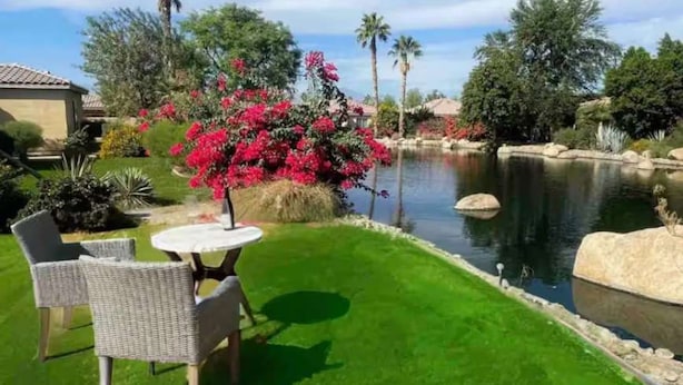 A well-maintained garden with a pond, a table with chairs, and various plants and trees.