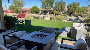 An outdoor patio with seating, a fire pit, and a view of a landscaped garden and pool.
