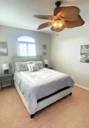 A bedroom with a bed, nightstands, a ceiling fan, a window, and wall art. - Country Club Home With Lakeside Views Golf (Indio)
