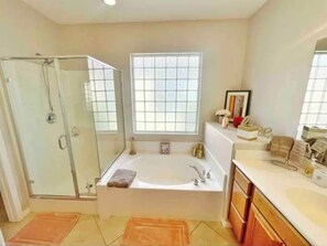 A bathroom with a glass shower enclosure, a large bathtub, a window, and wooden cabinets. - Country Club Home With Lakeside Views Golf (Indio)