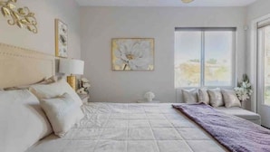 A bedroom with a large bed, a window with a view, and a decorative wall piece.