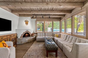 A living room with a stone fireplace, a large sofa, and a television on the wall. - Private Oasis Retreat (Palm Springs)