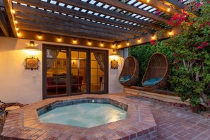 A hot tub with a brick border, a covered patio with string lights, and two wicker chairs. - Private Oasis Retreat (Palm Springs)