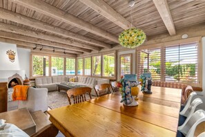 A spacious room with a wooden ceiling, large windows, a fireplace, and a dining table with chairs. - Private Oasis Retreat (Palm Springs)