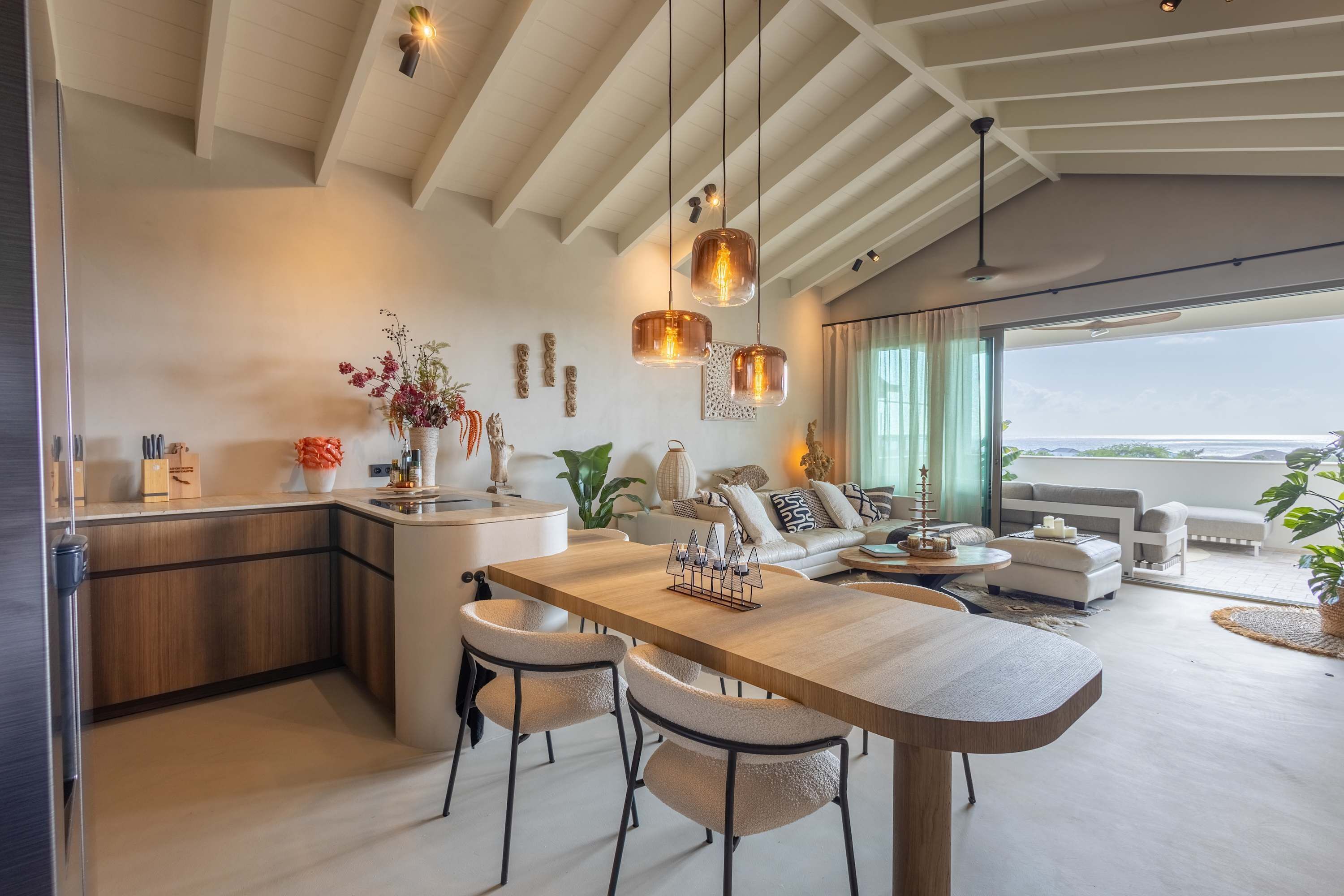 Cozinha moderna com ilha central, área de refeições com cadeiras e sala de estar com sofá e mesa de centro.