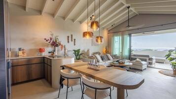 Cozinha moderna com ilha central, área de refeições com cadeiras e sala de estar com sofá e mesa de centro.