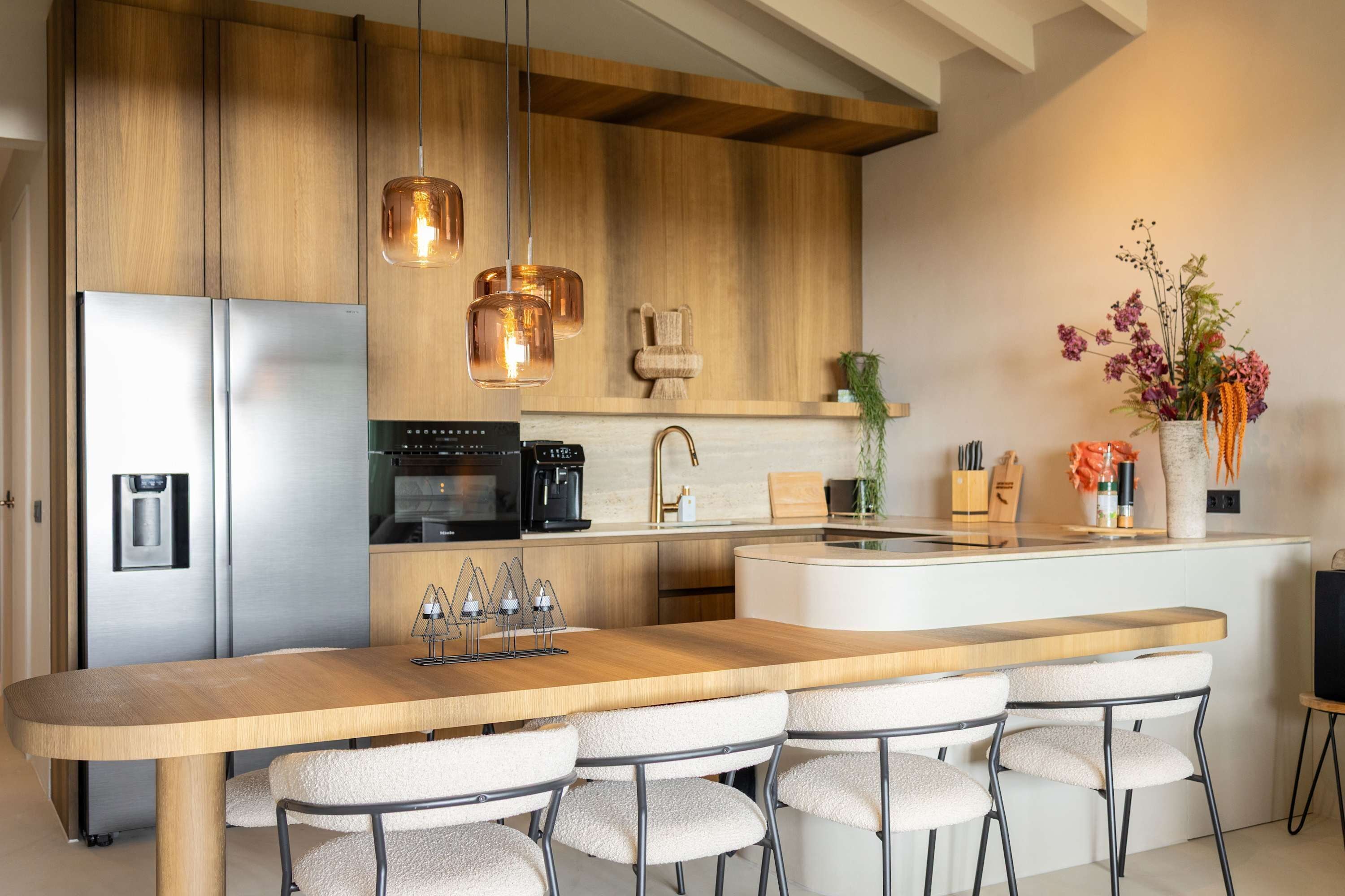 Cozinha moderna com geladeira de aço inoxidável, máquina de café e ilha de madeira com banquetas.