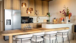 A modern kitchen with a stainless steel refrigerator, a coffee machine, and a wooden island with bar stools. - Aurel 13 Ocean View Penthouse at The Reef (Sint Michiel)