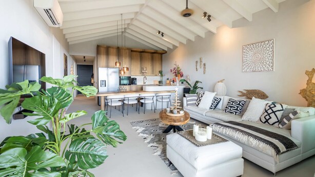 A modern living space with a kitchen, dining area, and a white sofa with patterned cushions. - Aurel 13 Ocean View Penthouse at The Reef (Sint Michiel)