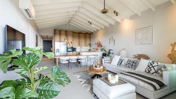 Um espaço moderno com cozinha, sala de jantar e um sofá branco com almofadas estampadas.