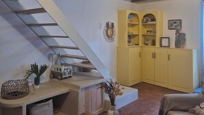 Une pièce avec un escalier, des poutres en bois, un buffet jaune et une table sur laquelle se trouve un vase.