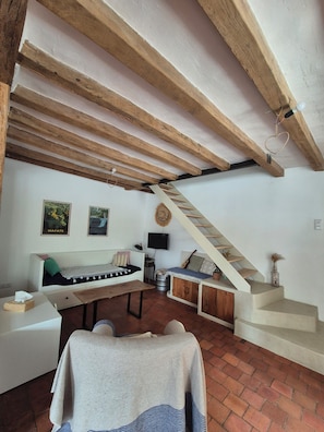Una habitación rústica con vigas de madera a la vista, una escalera, un sofá, una mesita y un televisor.