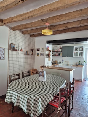 Un comedor con mantel a cuadros, sillas de madera, una lámpara colgante y una cocina al fondo.