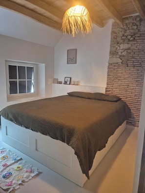 Un dormitorio con cama, ventana, un cuadro en la pared y una pared de piedra.