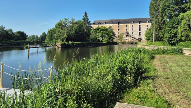 Une vue sur le bord de la rivière, avec un bâtiment, des espaces verts et une barrière faite de cordes.