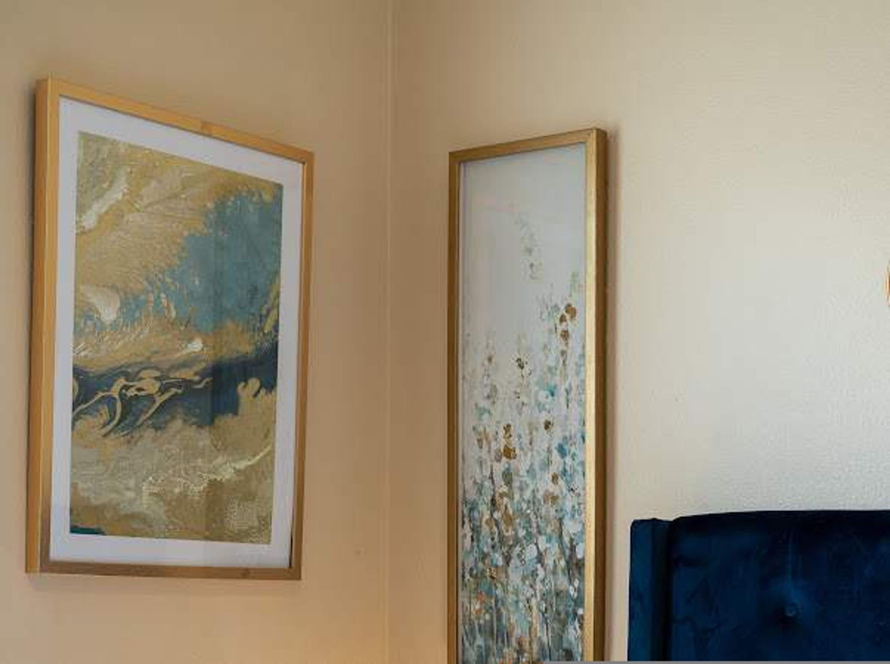 Une pièce avec un lit, deux œuvres d’art encadrées et un mur uni.