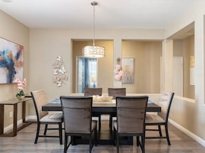 A dining room with a rectangular table, six chairs, a chandelier, and decorative wall art. - Pools Golf and Tennis Home (Indio)